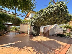 A courtyard with a tiled floor, a covered seating area, and a staircase leading to a building.
