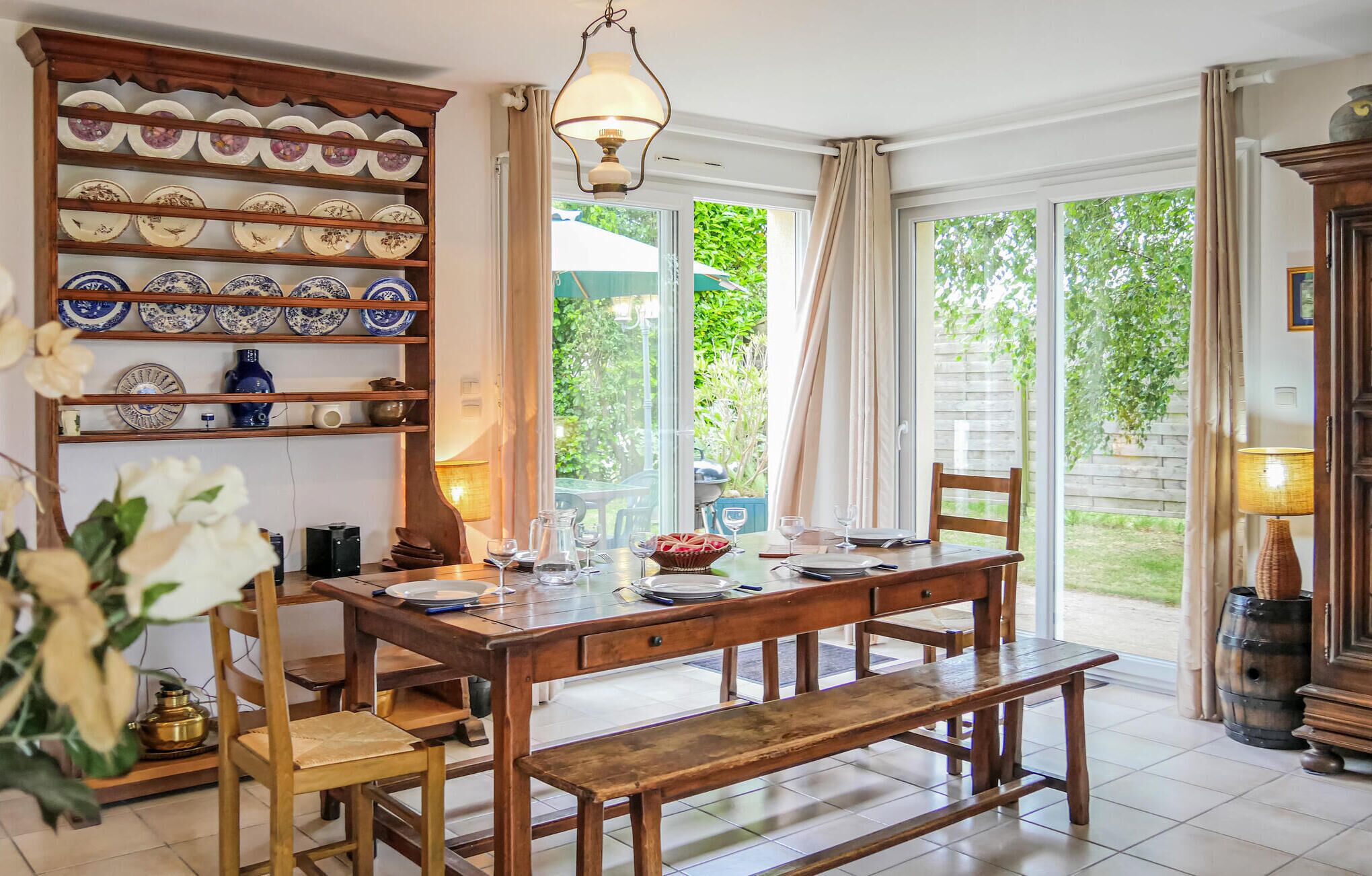 Un coin repas avec une table en bois dressée pour quatre personnes, entourée de chaises. Un grand meuble en bois orné d’assiettes décoratives se trouve à gauche.