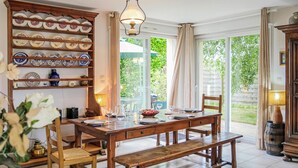 Un'area pranzo con un tavolo di legno apparecchiato per quattro persone, circondato da sedie. A sinistra, un ampio mobile in legno con piatti decorativi.
