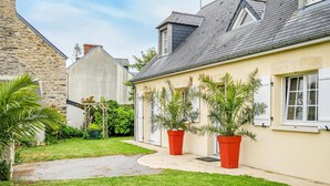 Una casa con facciata in pietra, tetto spiovente e un piccolo giardino con piante in vaso.