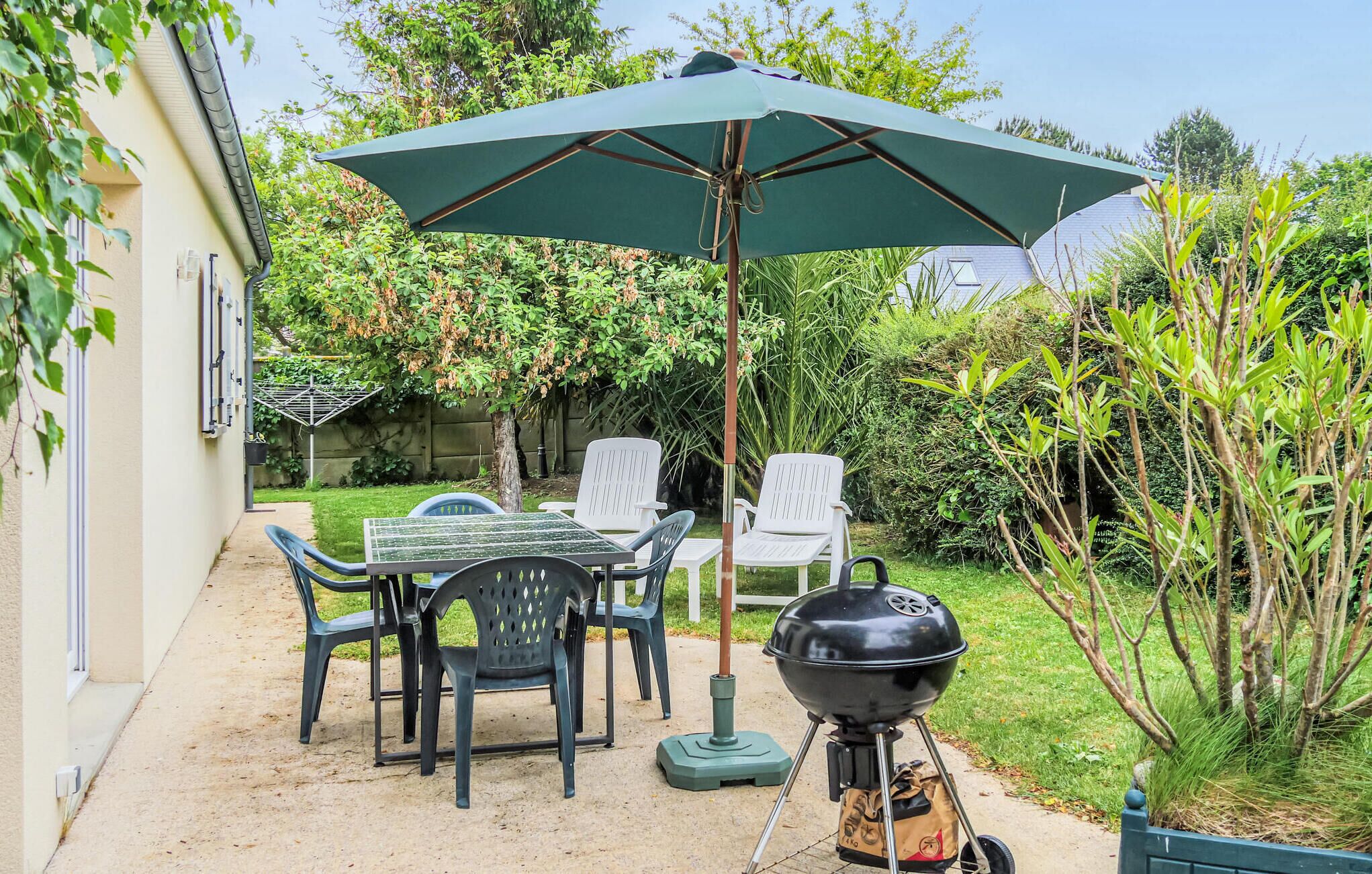 An outdoor patio with a table and chairs, a barbecue grill, and a large umbrella.