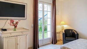 Una camera d'albergo con una televisione a parete, un tavolino con un vaso di fiori, una sedia e una lampada.