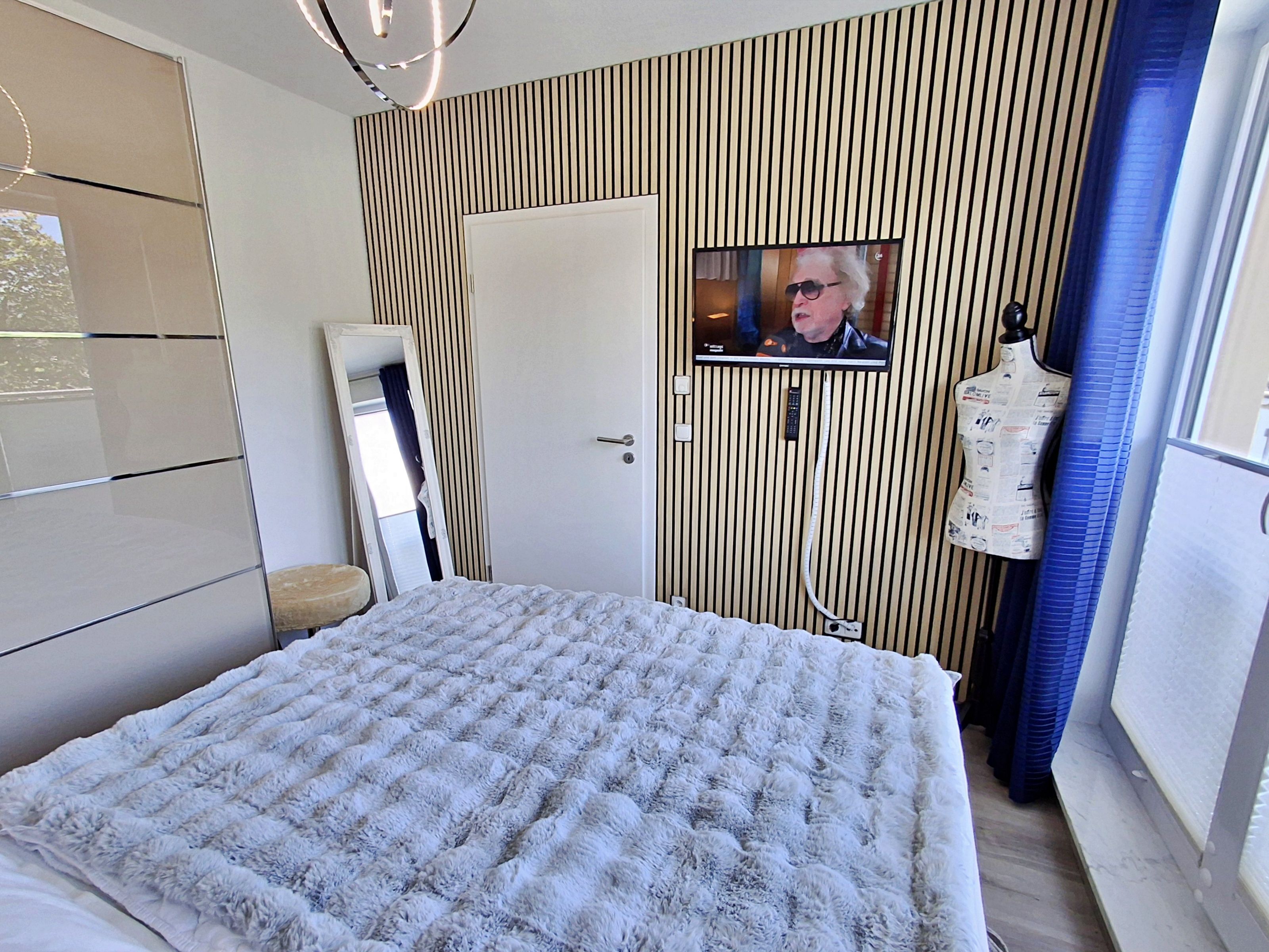A bedroom with a bed, a television mounted on the wall, a wardrobe, and a mirror.