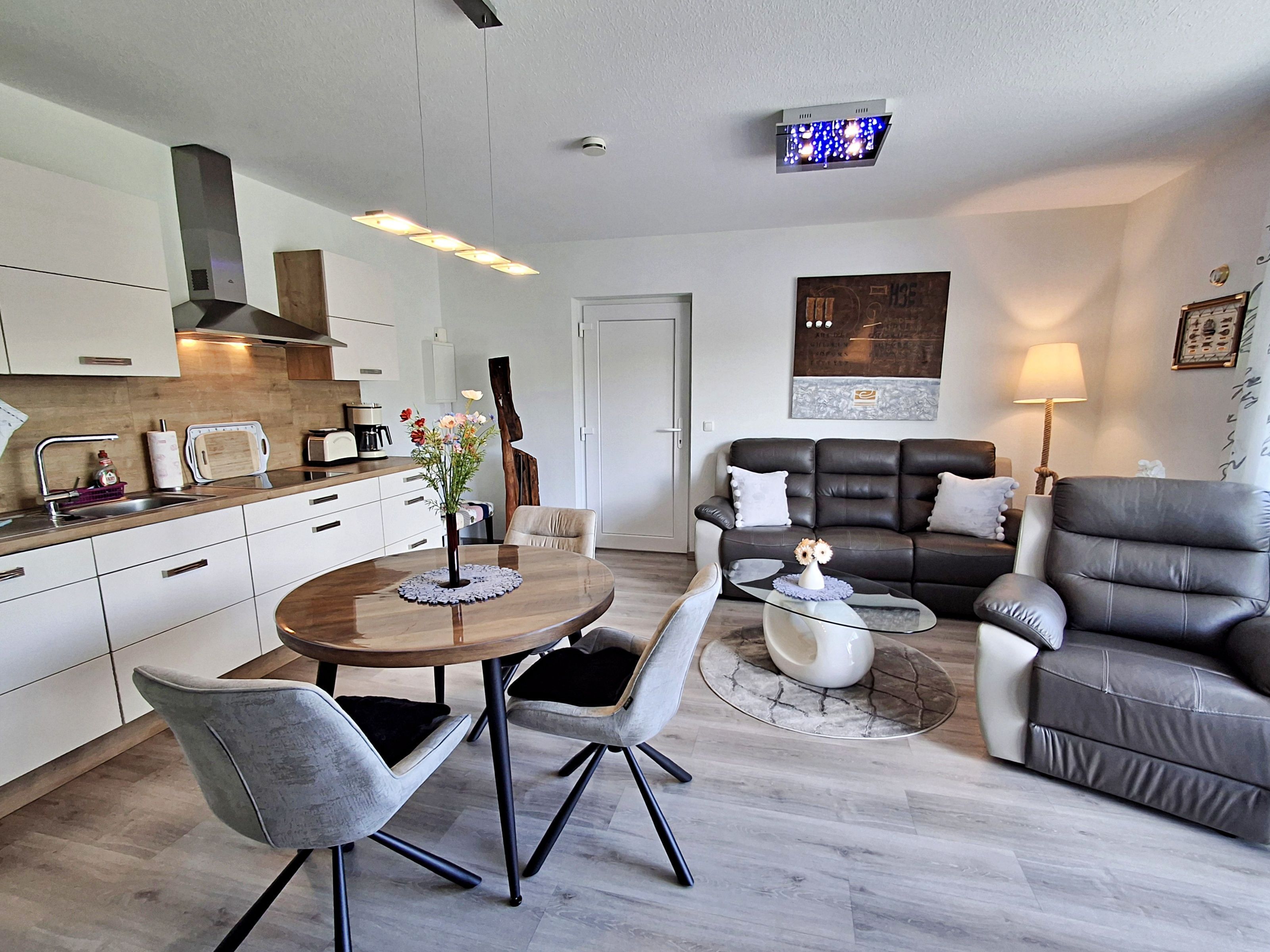 A modern kitchen with white cabinets, a dining table with chairs, a sofa, and a coffee table.