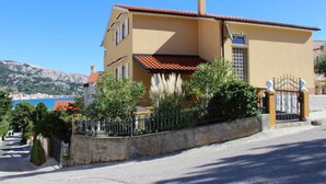A two-story building with a red-tiled roof, a yellow facade, and a gated entrance. - Holiday apartment with terrace (Baška)