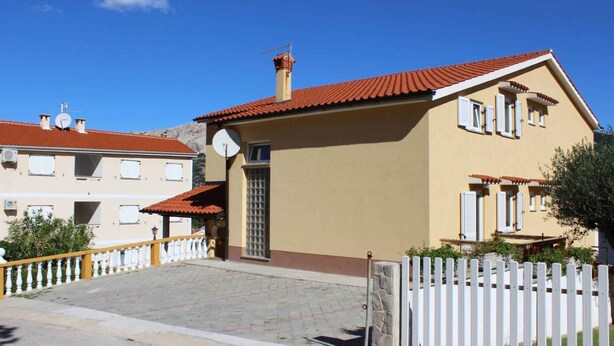 Un edifici de dues plantes amb teules vermelles, façana beix i una tanca de piquets blancs.