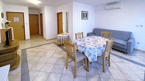 A dining area with a round table and four chairs, a sofa, and a TV on a stand. - Holiday apartment with terrace (Baška)