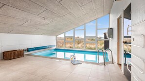 Ein Schwimmbecken mit klarem, blauem Wasser, einer Holzbank und Blick ins Freie durch große Fenster.