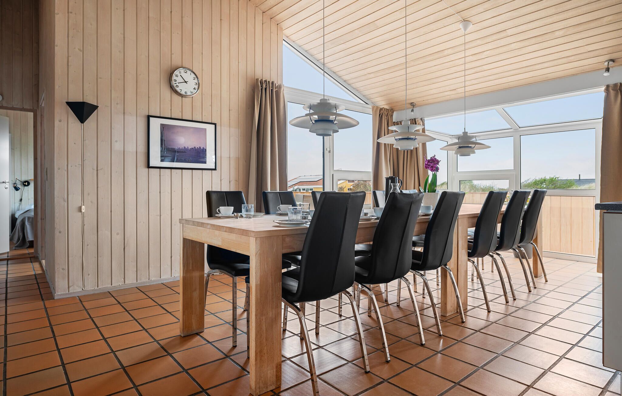 A dining area with a wooden table and chairs, a clock, and a framed picture on the wall.