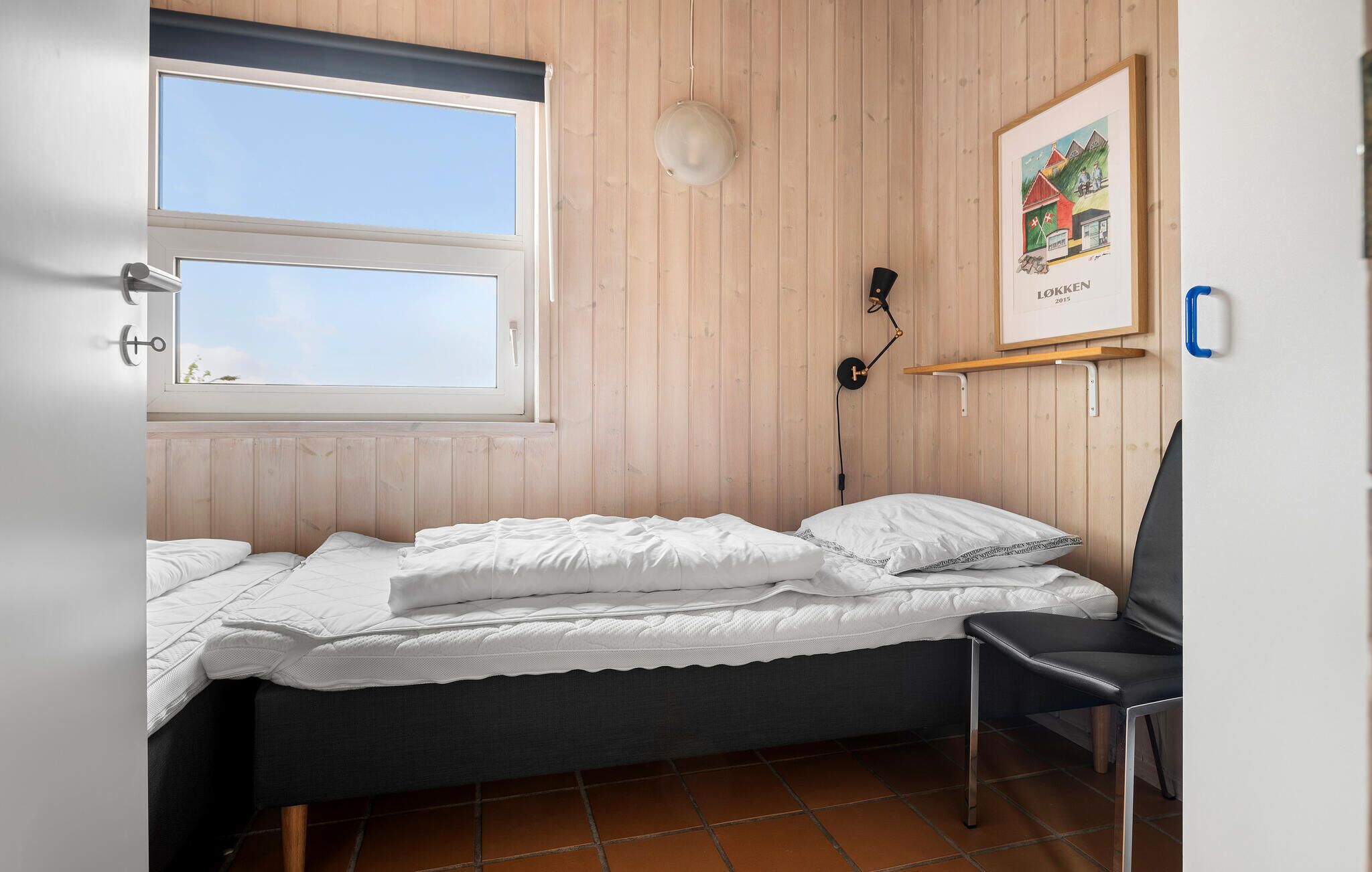 Ein kleines, gemütliches Schlafzimmer mit einem Einzelbett, einem Sessel, einem Fenster und einer Wandleuchte.