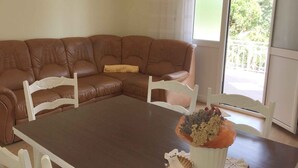 Una sala de estar con un sofá de cuero marrón, una mesa de comedor de madera y una silla blanca.