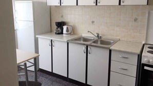 Cocina compacta con armarios blancos, un lavamanos doble, cafetera y una pequeña mesa.