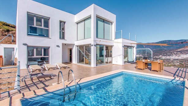 Un edificio moderno blanco con piscina, asientos al aire libre y vistas del paisaje.