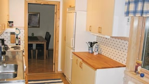 Cocina compacta con encimera de madera, refrigerador, pileta y zona de comedor visible a través de una puerta abierta.