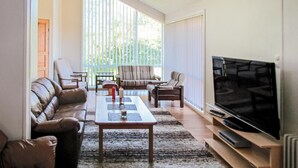 Una sala de estar con sofá, sillones, una mesa de centro y un televisor sobre un mueble.