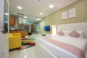 A hotel room with a large bed, a yellow armchair, a kitchenette, a television, and artwork on the walls. - Piks Key - Spring Tower (Dubai)