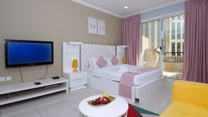Une chambre d’hôtel moderne dotée d’un grand téléviseur à écran plat, d’un lit confortable avec une tête de lit blanche, d’une table de chevet avec une lampe et d’une petite table ronde sur laquelle se trouve un bol de fruits.