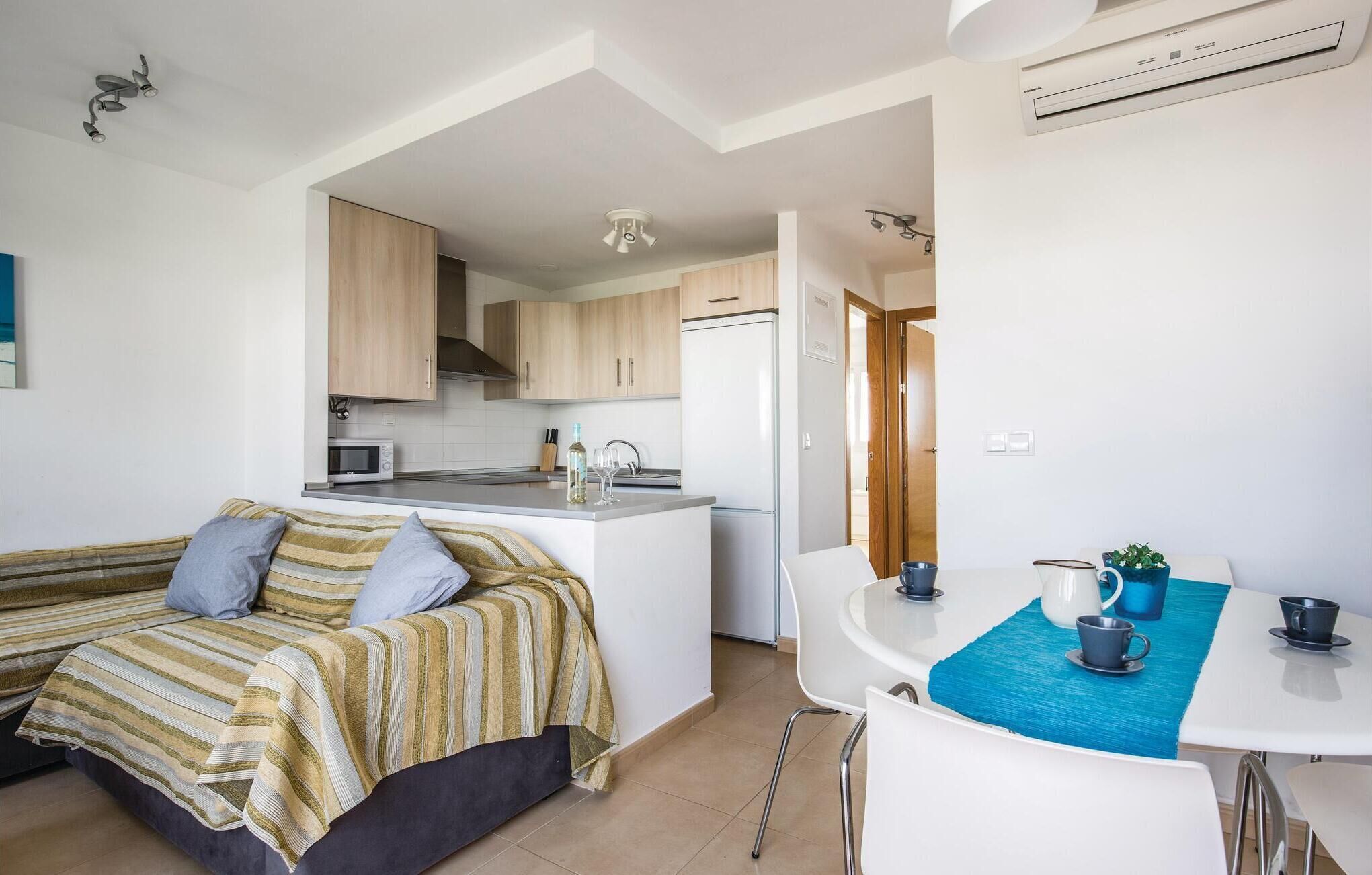 A compact living space with a kitchenette, a sofa with a striped blanket, a dining table with a blue placemat, and a coffee maker.