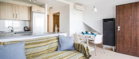 Una cocina moderna con refrigerador incorporado, un comedor con mesa y sillas, y un sofá a rayas con almohadones.