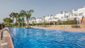En swimmingpool med kristallklart blått vatten, omgiven av vita byggnader och palmer.