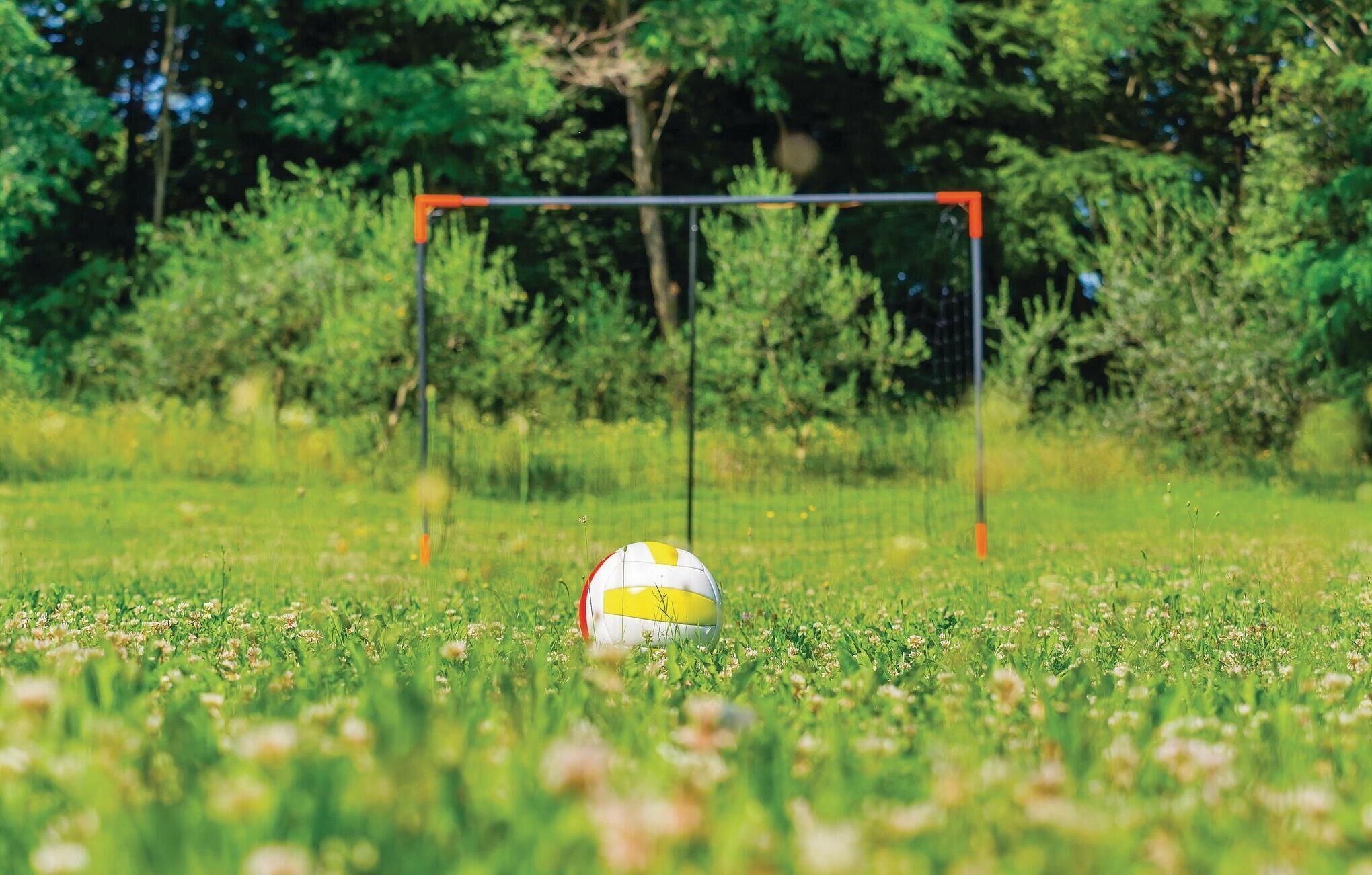 Un ballon de volley-ball sur un terrain herbeux, avec un poteau de but en arrière-plan.