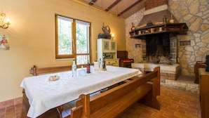 A dining area with a wooden bench, a table with a white tablecloth, a stone fireplace, and a window with blinds. - Nice home in Nedescina (Nedescina)