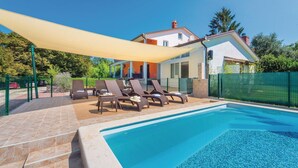 A swimming pool with lounge chairs and a shaded area, surrounded by a fence and a house in the background. - Nice home in Nedescina (Nedescina)