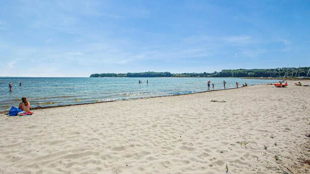 Une plage où l’on voit des gens se baigner et se promener le long du rivage.