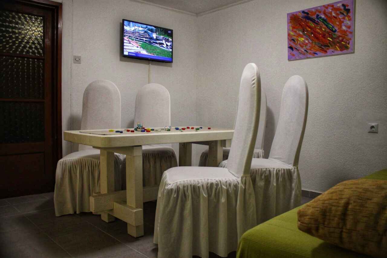 Una habitación con una mesa, cuatro sillas, un televisor en la pared y un cuadro abstracto de colores.
