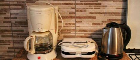 A kitchen with a coffee maker, a kettle, and a portable charger on the counter.