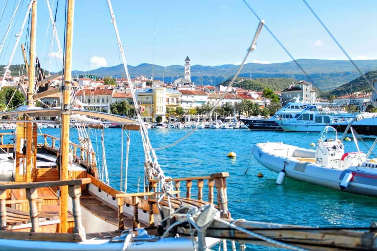 Ein Yachthafen mit vertäuten Booten, im Hintergrund eine Stadt und ein markanter Turm.