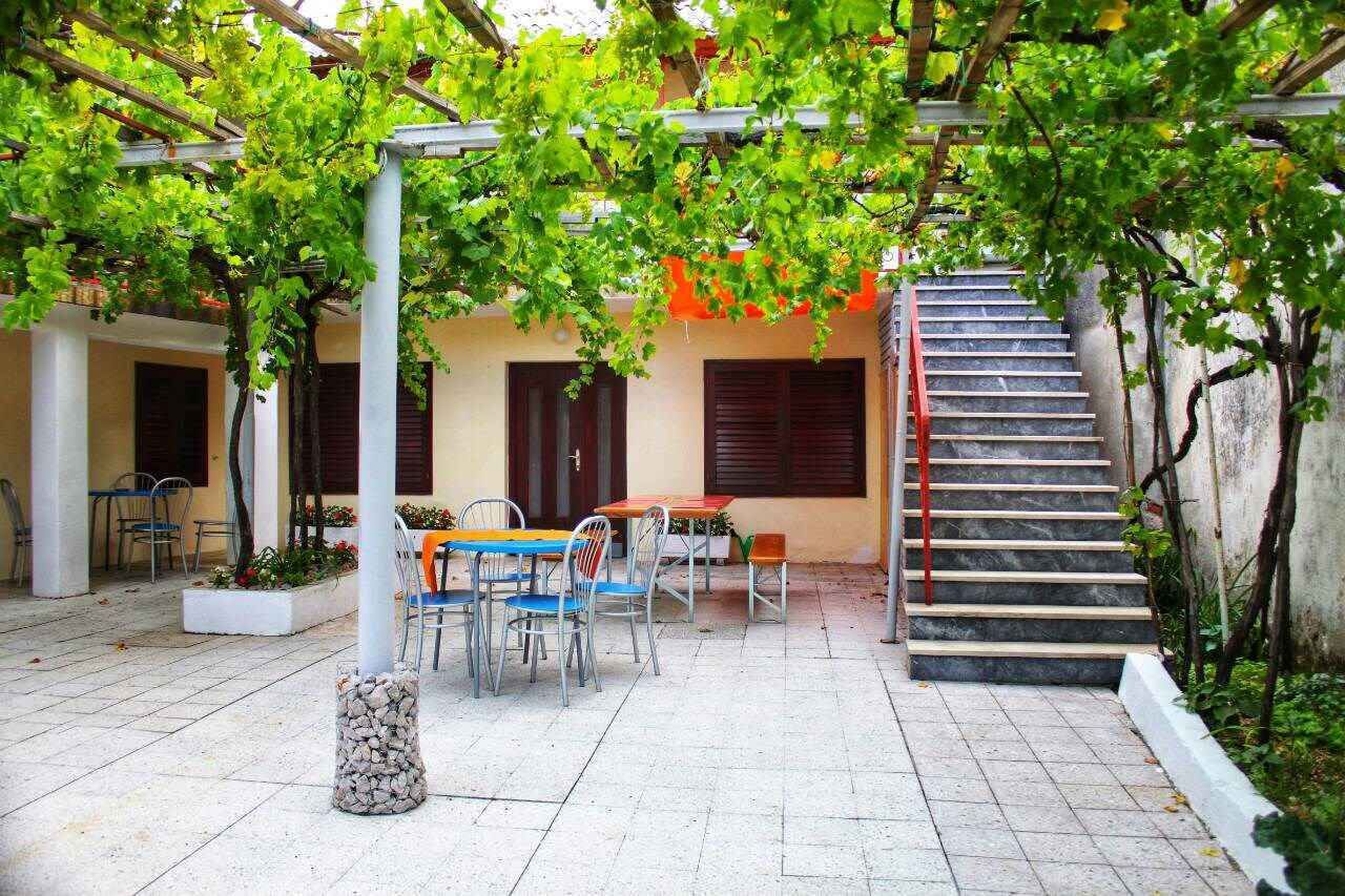 A covered outdoor area with a table and chairs, a staircase, and a pergola with green foliage.