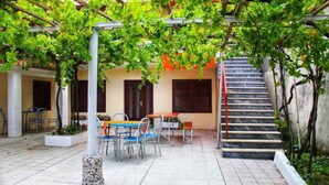 A covered outdoor area with a table and chairs, a staircase, and a pergola with green foliage.