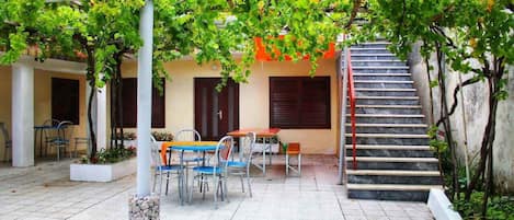 A covered outdoor area with a table and chairs, a staircase, and a pergola with green foliage.