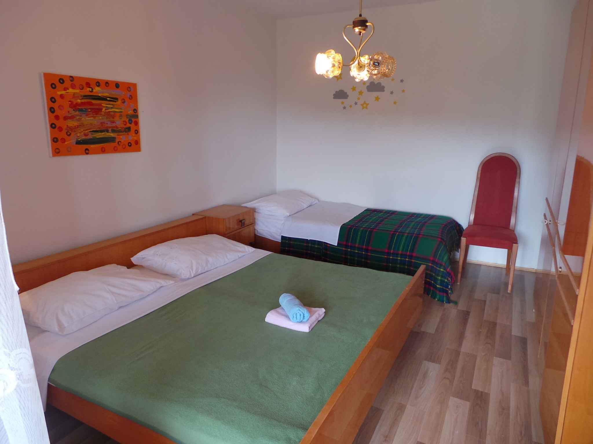 A room with two single beds, a wooden nightstand, a red chair, and a ceiling light fixture.