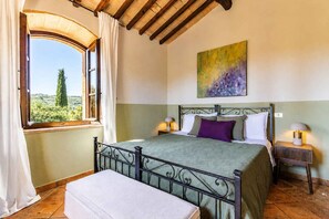 Un dormitorio con cama, ventana con cortinas, un cuadro en la pared y una mesita de noche con lámpara.