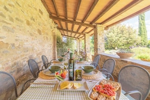 Un espacio de comedor al aire libre con muros de piedra, una pérgola y vistas a la vegetación.