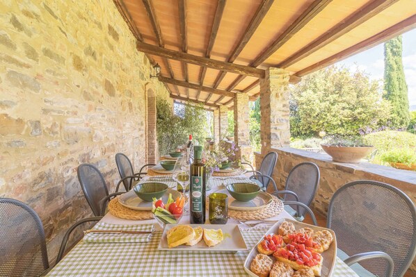 An outdoor dining area with stone walls, a pergola, and a view of greenery.