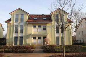 Un edificio residenziale a due piani con facciata simmetrica, ingresso centrale e un piccolo giardino antistante.