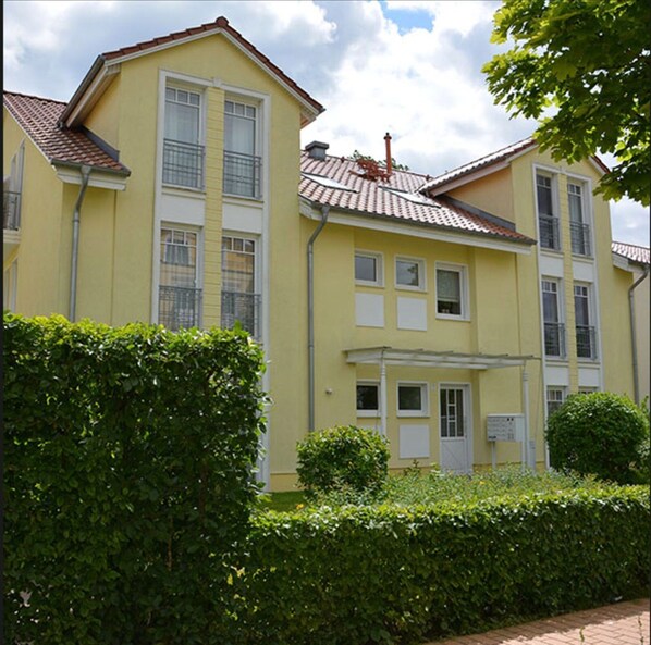 Un edificio giallo su due piani, con tetto in tegole, diverse finestre e un ingresso coperto.