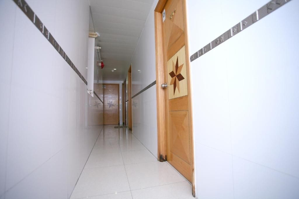 A corridor with a wooden door featuring a star design, white walls, and a tiled floor.
