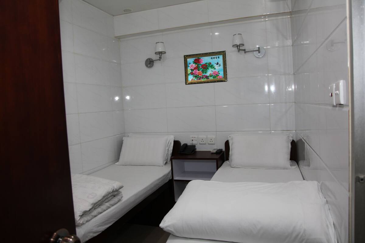 A hotel room with two single beds, a small table with a phone and a lamp, and a wall-mounted picture.
