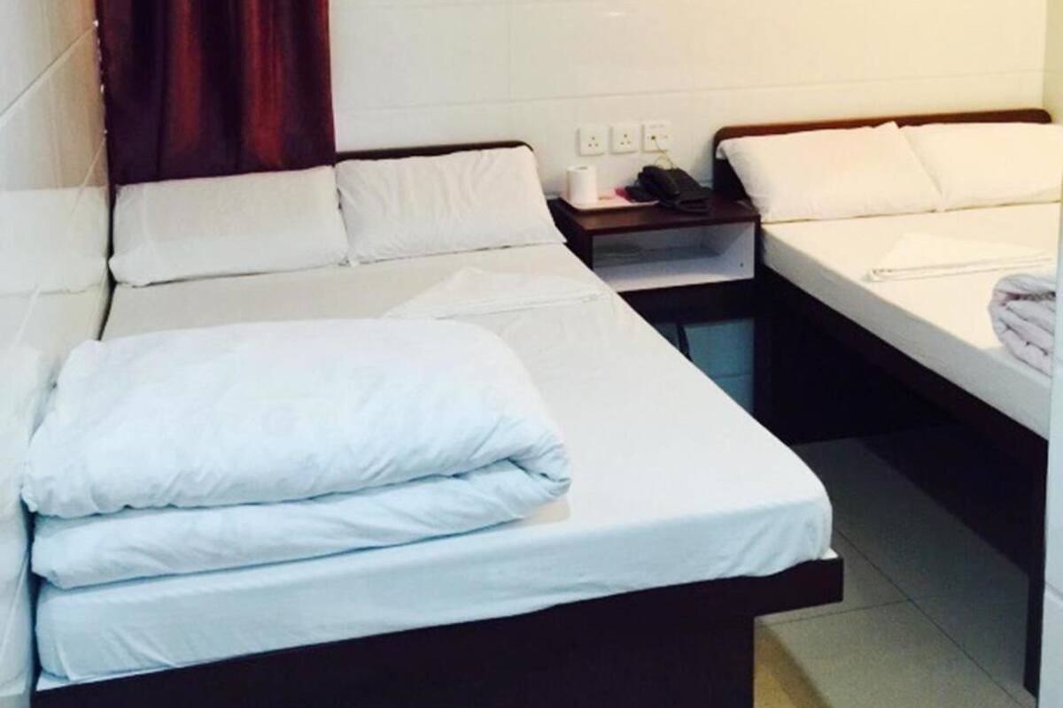 A hotel room with two beds, a small table, and a nightstand with a phone and a bottle.