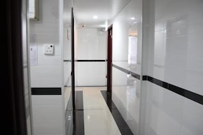 Un pasillo con paredes de azulejos blancos, una franja negra y una puerta al final.