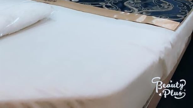 A bedroom with a bed, pillows, a wall-mounted air conditioner, and a curtain.