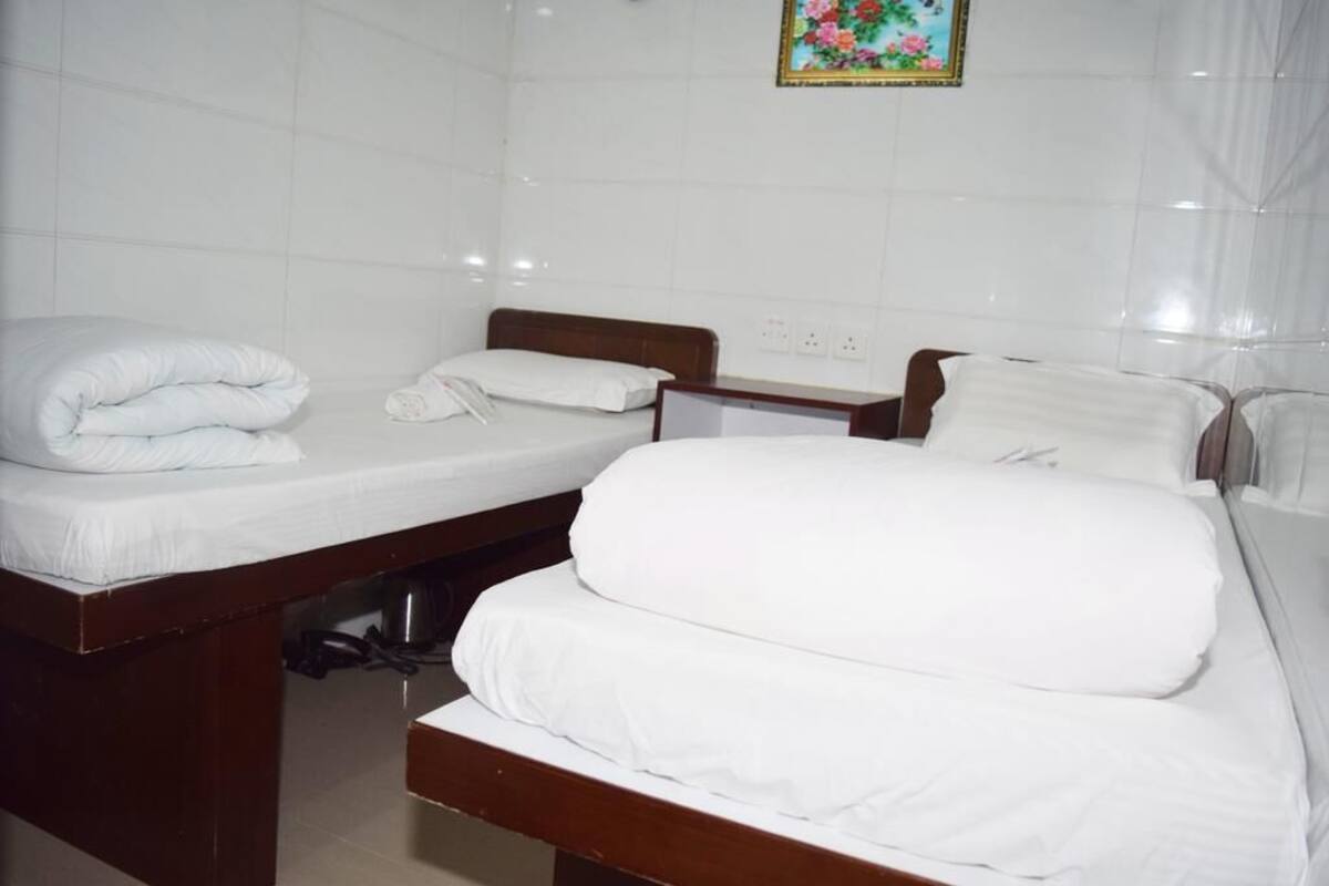 A hotel room with two beds, white bedding, and a tiled wall with a floral painting.
