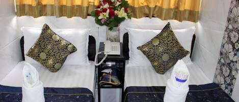 A hotel room with a bed, pillows, a bedside table with a phone, and a vase with flowers.