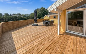 Eine Holzterrasse mit Tisch und Stühlen, ein überdachter Außenbereich und eine Glastür, die in einen Innenraum führt.