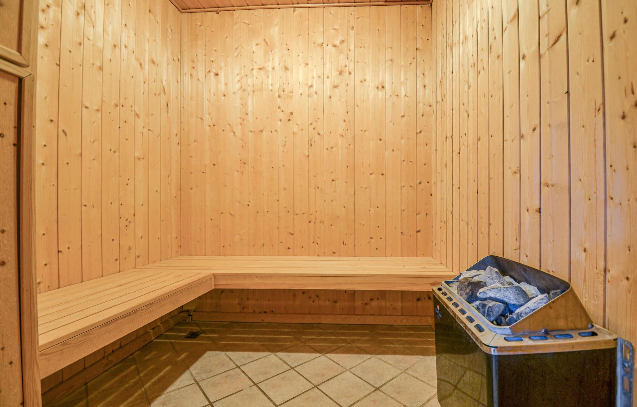 A sauna room with wooden walls and a bench. There is a sauna heater on the floor.