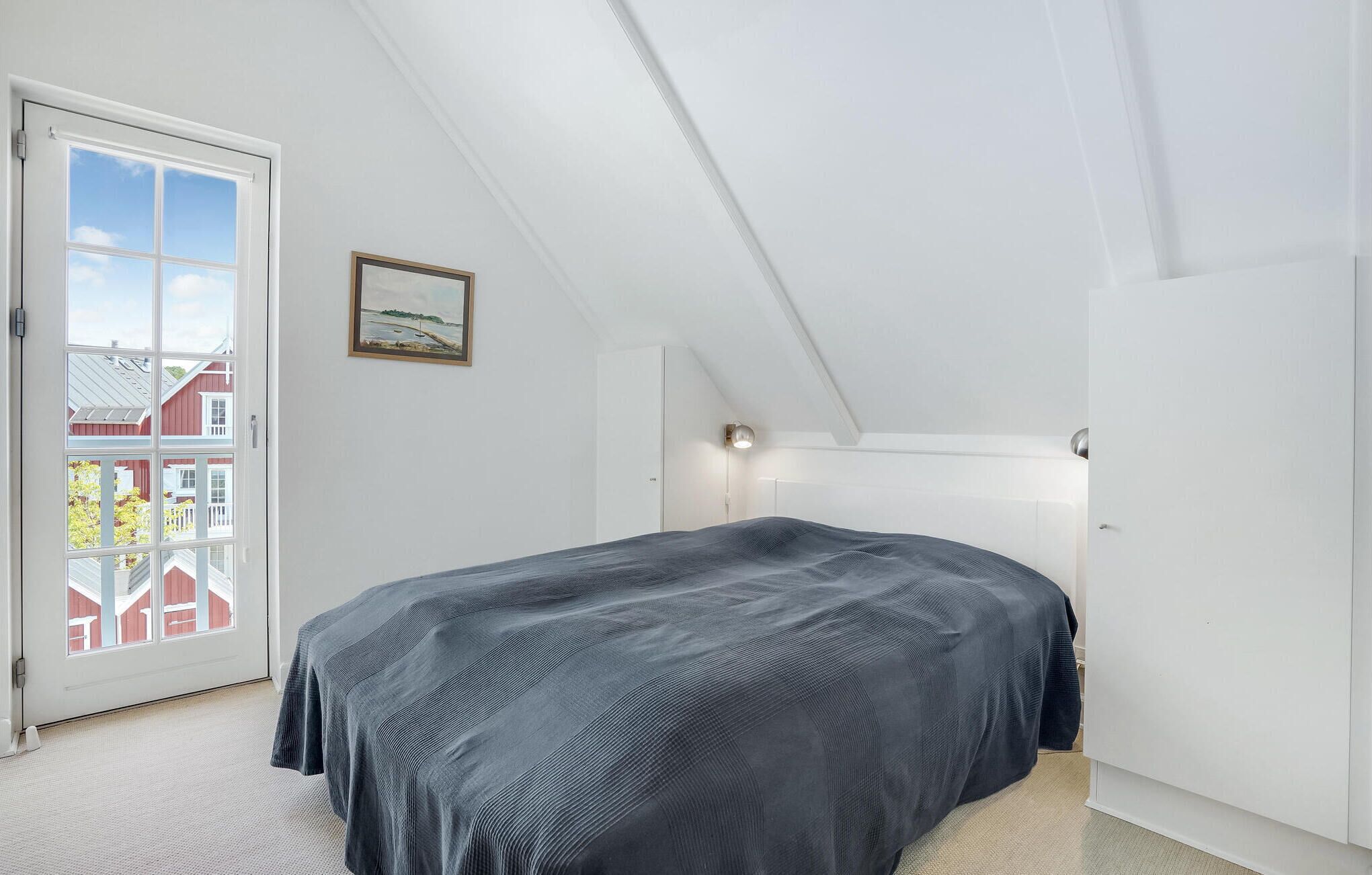 A bedroom with a large bed, a door with a view, a framed picture on the wall, and a ceiling light.